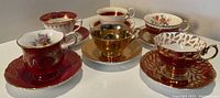 Front view of six assorted teacups with saucers placed in a group, showing variety in design and color.