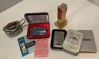 Photo showing six assorted lighters including boxed Zippos and Ronson lighter in case, silver-tone decorative lighter holder.