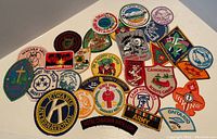 Photo showing a collection of 30 embroidered badges with Boy Scout themes and other community organizational patches, laid out on a white surface.
