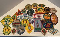 Photo showing 28 assorted embroidered cloth badges related to Boy Scouts and Canadian scouting events arranged on a flat surface.