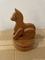 Side view of wooden cat figurine with visible painted eyes and whiskers, sitting on circular music box base