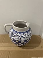 Photo showing ceramic vase with handle, blue and white geometric pattern, with chip on rim.