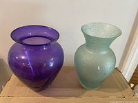 Two opaque glass vases - purple with wide neck, and aqua blue crackled textured with flared neck.