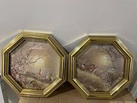 Two octagonal framed art pieces side by side showing a chapel with blossoming tree and a countryside landscape with animals