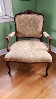 Front view of vintage decorative accent chair with carved wooden frame and palm leaf patterned beige upholstery.