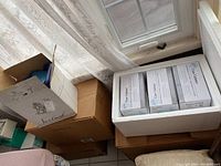 Photo showing stacked boxes including Care Cather catheter supplies in white boxes in styrofoam packaging beside window.