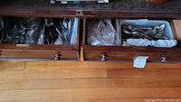 Two wooden drawers filled with assorted stainless steel eating utensils including forks, knives, and spoons. Items are visibly worn.