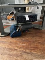 Overview of Denon audio receiver and speaker under TV stand with blue box containing cables.