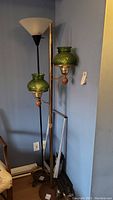 Overview of two floor lamps in the corner. Left is black metal with plastic shade; right is gold toned metal with two green bubble glass shades.