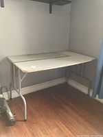 Plastic folding table shown set up in corner of room with a glass piece laid out on top.