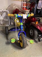 Front view of kids training wheel bike showing wide front tire, yellow pedals, and colorful decal on handlebars