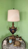 Full view of vintage urn style lamp with shade, small clock and various candle holders, tray on marble table