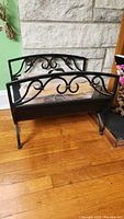 Front and side views of a black metal fire wood log holder with decorative scroll metalwork and noticeable rust spots.