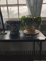 Two vintage planters side by side on a black table near a window, one with a live plant trailing over the edge.