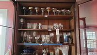 Wooden shelves holding a variety of clear and blue glass stemware and bowls, showing overall grouping and quantity.