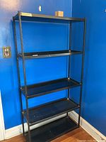 Full front view of the black metal storage rack with 5 shelving levels against a blue wall.