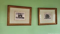 Two framed black and white French theme architectural prints side by side on a green wall, ornate gold-toned frames visible with matting.
