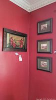 Four framed artworks hanging on red wall; one larger monk image and three smaller equestrian hunt scenes stacked vertically