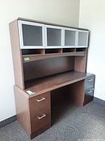 Front view of brown wood desk unit with four drawers and a hutch with four cabinet doors with frosted glass inserts.