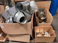 Boxes filled with assorted galvanized metal vent duct components including cylinders, elbows, and other shapes, some with mesh/grille inserts.