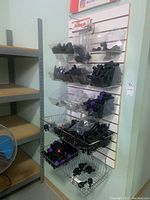 Wall-mounted display with multiple plastic bins containing black plastic pipe fittings of various types, some with purple caps.