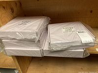 Stacked five shrink-wrapped white boxes on a wooden shelf.