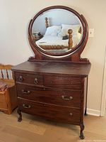 Front view of dark mahogany lowboy dresser with round bevelled mirror reflecting a bed, showing four drawers with original metal drawer pulls, some missing.