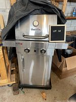Front view of Char-Broil Commercial propane BBQ grill with black cover partially draped on top, showing thermometer, control knobs, and propane tank storage compartment.