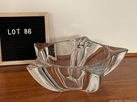Clear star shaped glass bowl on wooden surface with a black letter board reading LOT 86 in the background. Angle shows the curved edges and thickness of the glass bowl.
