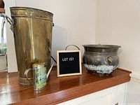 Photo showing the brass umbrella stand with ram motif, copper hanging flower pot with elephant motif, small brass watering can with print, and another smaller brass watering can on a wooden shelf.