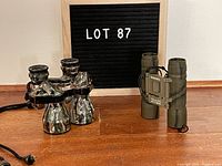 Both pairs of binoculars on a wooden floor with a sign 'Lot 87'