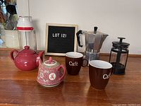 Photo of coffee and tea items on kitchen counter including two teapots, two mugs, stovetop espresso maker, and French press