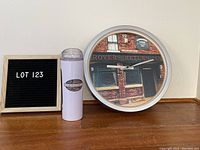 Full view of the round Rovers Return Inn clock and adjacent Coronation Street cup on a wooden surface with Lot 123 sign beside.