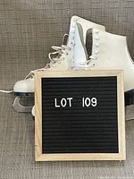 Pair of white Daoust women's figure skates with black heels and polished blades, next to lot number.