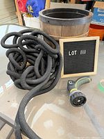 Coiled black expandable garden hose next to a multi-pattern spray nozzle on a glass table, with wooden bucket in background.