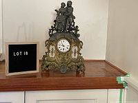Front view of the ornate metal clock with figurine on top showing full details and clock face with Roman numerals.