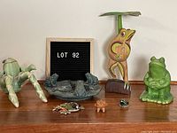 Photo showing the frog collection including the green ceramic frog, wooden frog with leaf, bird feeder with frogs, and smaller frog figurines.