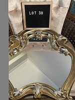Front view of gold and silver coloured mirror showing ornate curved frame with floral scrollwork and clear mirror surface.