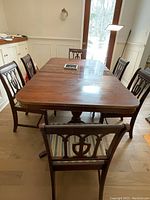 Rectangular mahogany dining table with 6 matching fiddle back style chairs around it. One captain's chair visible at end with arms and striped seat.