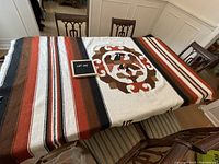 Top-down photo of vintage Mexican blanket spread over a dining table, showing eagle motif and striped pattern in earth tones.