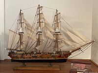 Three-masted wooden model ship Fragata Siglo XVIII with cream sails and rigging on wooden base, alongside smaller two-masted miniature ship in a glass case