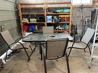Full view of rectangular glass patio table with metal frame and four matching metal chairs around it in storage space.