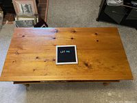 Top view of pine coffee table showing wear marks and natural wood finish with a lot number sign placed in center.
