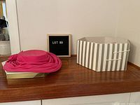 Photo of the pink hat resting on a box with the striped hat box nearby and a letter board showing lot number.