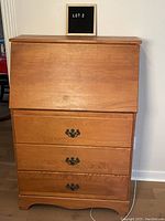 Front view of the closed secretary's desk showing the smooth wooden finish and three drawers with metal handles.