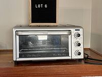 Front view of the silver T-fal toaster oven showing the glass door and black dials on the right side, placed on a wooden surface.