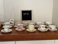 Photo of full set of 12 vintage teacups each with a matching saucer, plus extra saucers and unmatched cups in background.