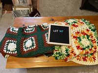 Two crocheted blankets placed side by side on a wooden table with a lot number sign