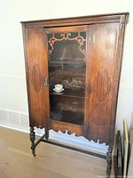 Full front view of vintage wooden china cabinet showing ornate glass door and carved details