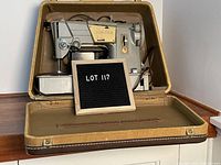 Side view of vintage Singer sewing machine inside an open brown hard case with fabric lining and latch closures, showing the machine resting securely inside the lid.